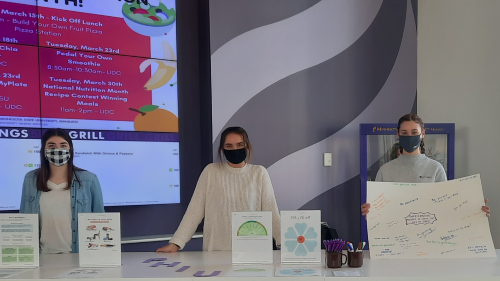 Four students wearing masks in the Dining Center posing in front of the Living Mindfully event