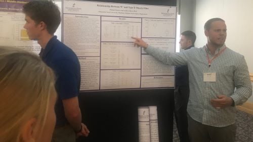An Exercise Science student pointing at his research board and explaning the data at a research event