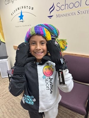 Child wearing a hat and mittens and grinning