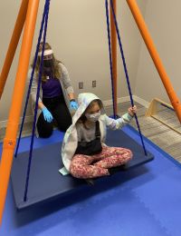 A student pushing a child on an indoor swing during a child language disorders session