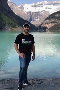 Brandon Carlson posing by a lake with mountains in the background