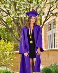 Zoya Parsi posing in cap and gown by a tree outside on campus