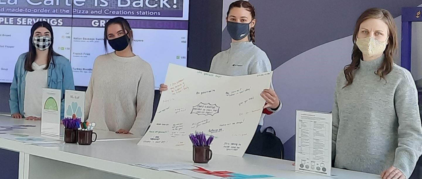 Four students wearing mask in the Dining Center participating in a health activity exhibit