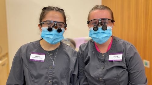 Lissette Garza and Kaitlyn Knutson with masks and magnification loupes in scrubs at dental clinic