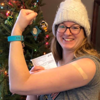 Nursing faculty with arm up showing vaccine card and band-aid on arm