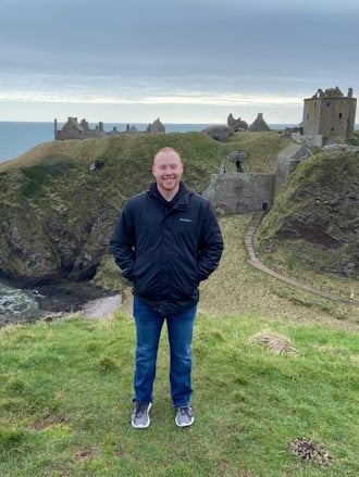 Man standing in front of a green landscape with cliffs and a castle
