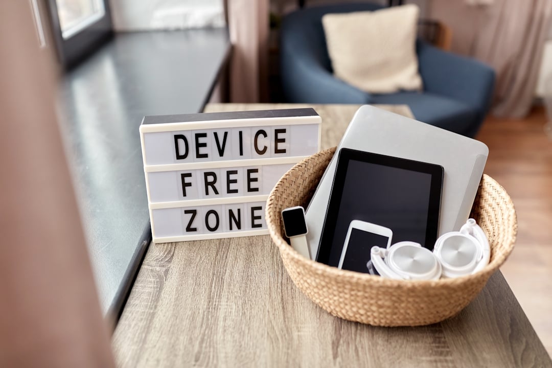 A basket containing electronic devices such as a cell phone, tablet, and headphones with a sign next to it that says 