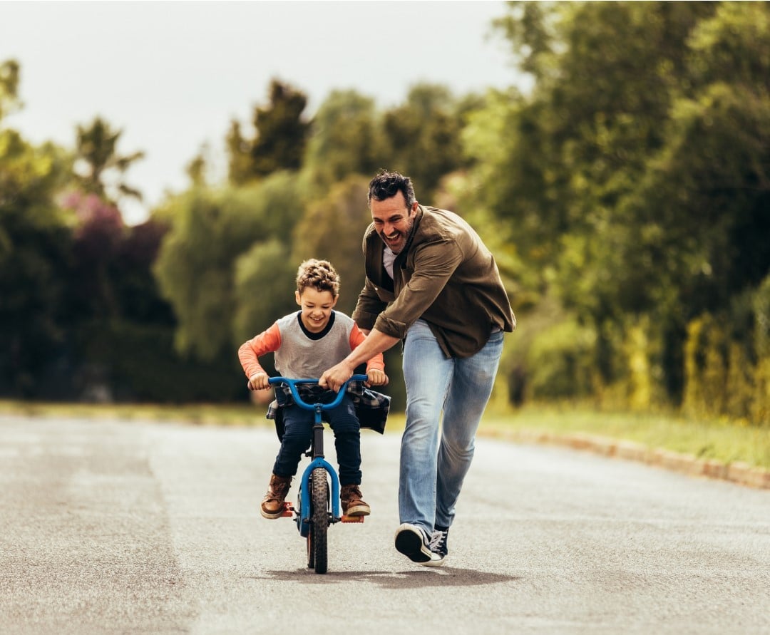 An adult running beside a kid learning how to ride a bike.