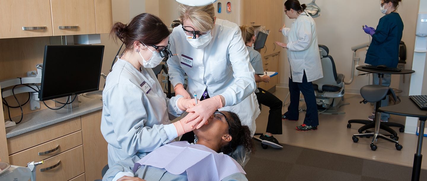 Instructor and student of advanced dental therapy working on a patient in the dental clinic with other students in the background