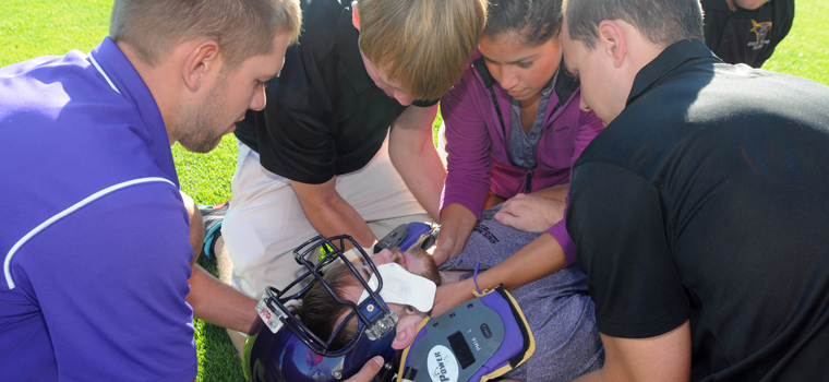 Athletic training faculty and students examining an injured athletic lying down on the field