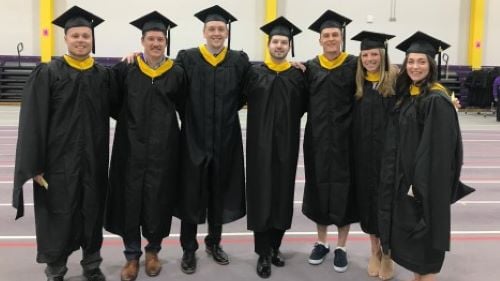 A group of Exercise Science students posing with caps and gowns at graduation