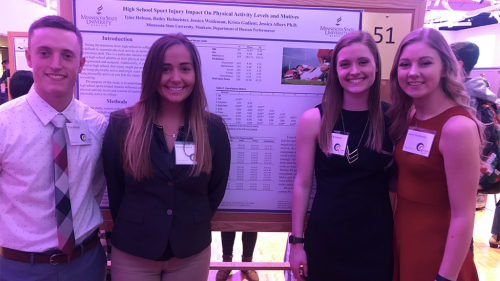 A group of Exercise Science students posing in front of there research board on high school sport injury impact on physical activity levels and motives at a convention