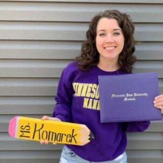 Madisyn Komarek posing next to a wall holding her Minnesota State University Mankato diploma