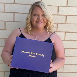 Haley Schaff posing by a wall holding her Minnesota State University Mankato diploma