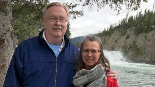 Bill Anderson with his wife Robin posing outside in front of a river