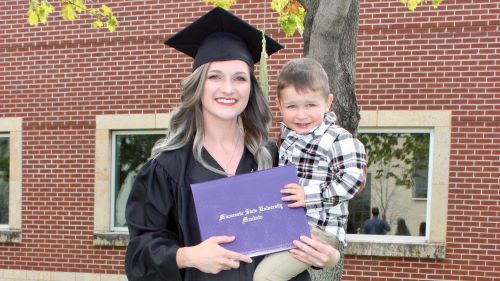 Kelsey Joines and her son posing outside at her graduation with diploma
