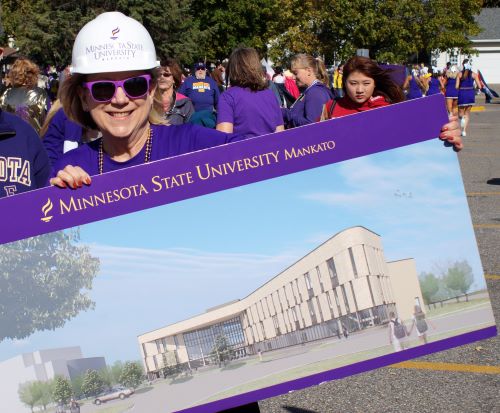 Dean Kris walking in the parade holding a banner of the new Clinical Sciences Building