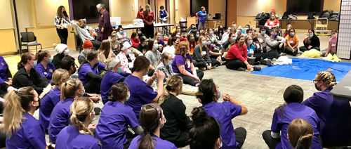 A large group of nursing students sitting on floor debriefing after mock disaster drill 
