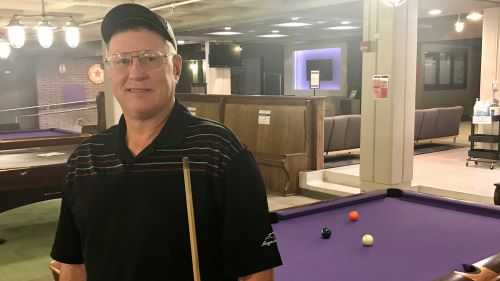 Jeff Maurer with a pool cue standing in front of a pool table in the MNSU bullpen