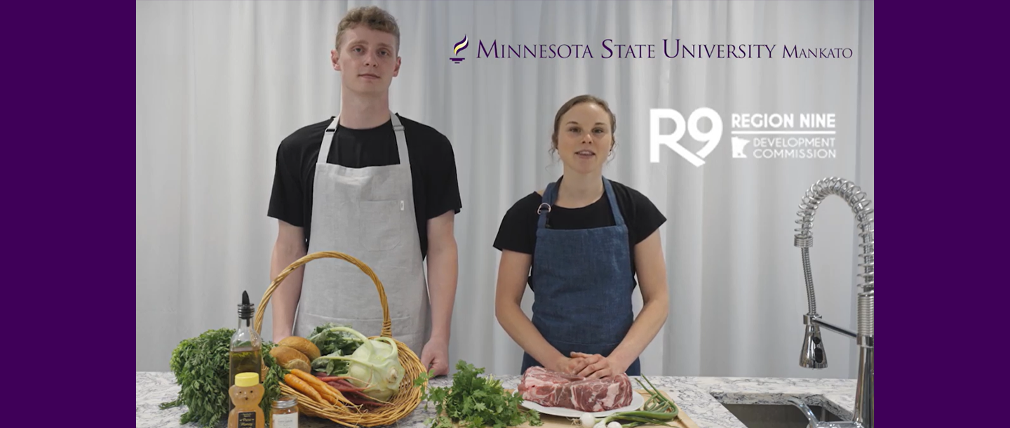 Two Dietetics students wearing aprons at kitchen counter with food on it. 