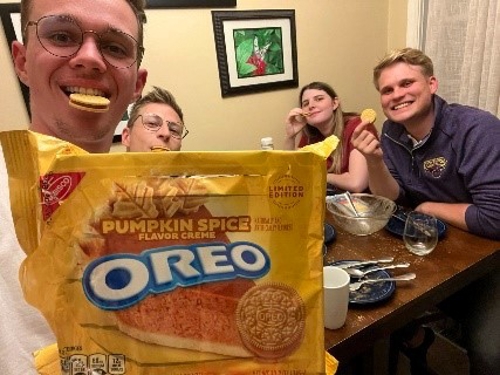 Four Austrian students, three sitting at a table and one standing up, enjoying Pumpkin Spice Oreo cookies