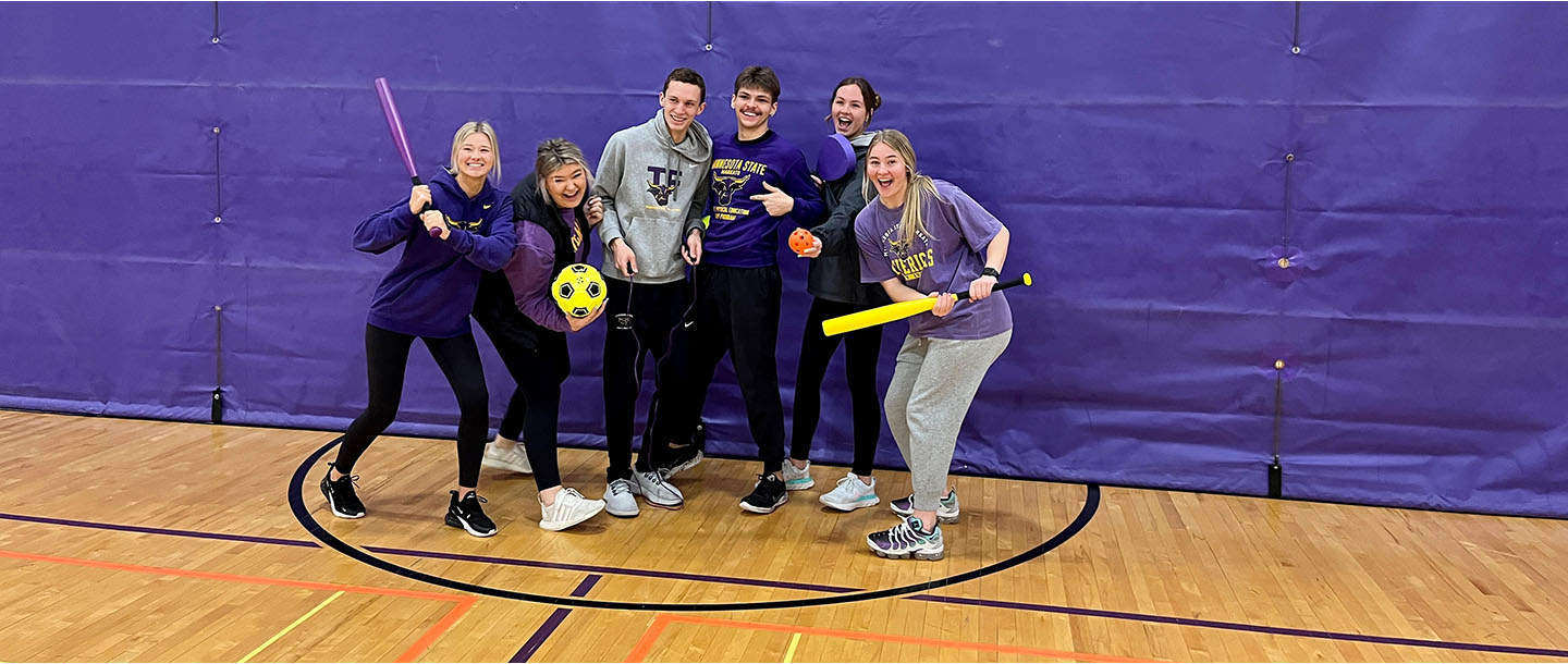 Six students posing in the gym with Maverick gear and sports equipment