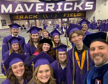 Group of students in caps and gowns in front of a MAVERICKS sign