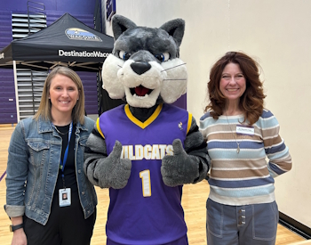 Two women standing with a mascot in a Wildcats jersey