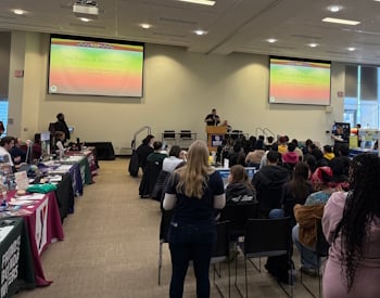 Auditorium containing attendees with a presentation showing on screens