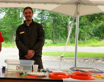 A college senior standing under a tent behind a table at an outdoor event.