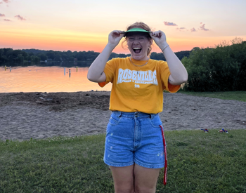 A young college student standing on the beach at sunset with a big smile of joy.
