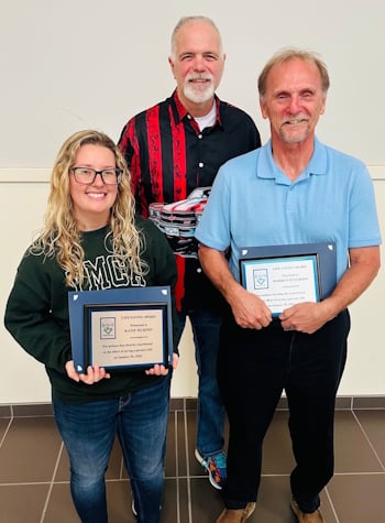 Photo of two people holding awards with a third person behind them