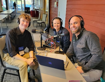 Three people wearing headphones at a table containing a laptop and microphones
