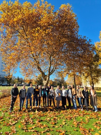 Group of people standing in front of a golden autumn tree with a blue sky in the background