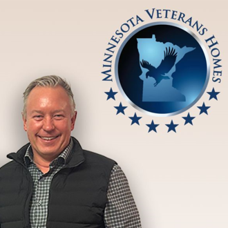 Profile photo of Eric Meittunen standing next to the Minnesota Veterans Homes logo on the wall