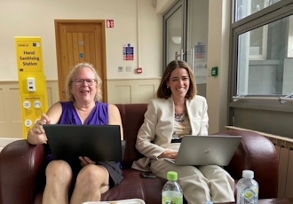 Two smiling women sitting on a sofa with laptops