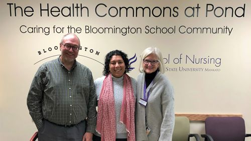 Three healthcare members posing in front of the Health Commons at Pond caring for the Bloomington school committee sign on the wall