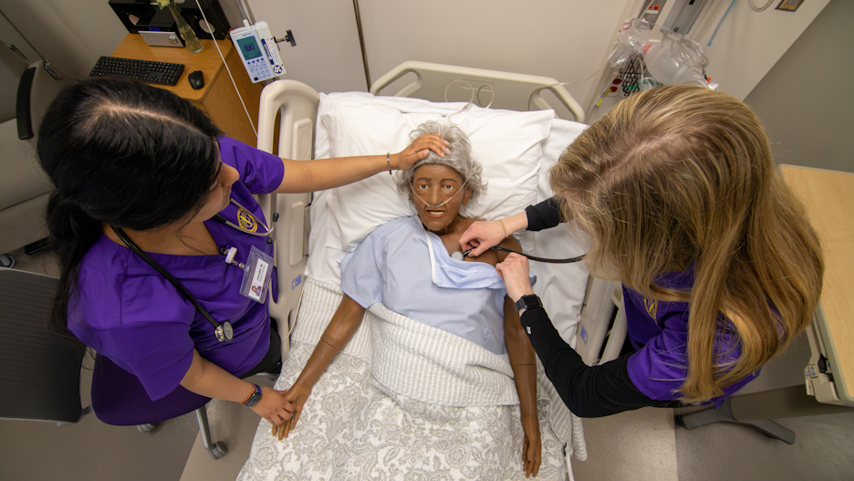 a group of people in purple scrubs and a personnequin in a hospital bed