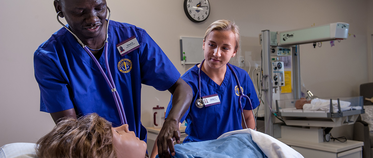 Two School of Nursing students examining a simulated patient
