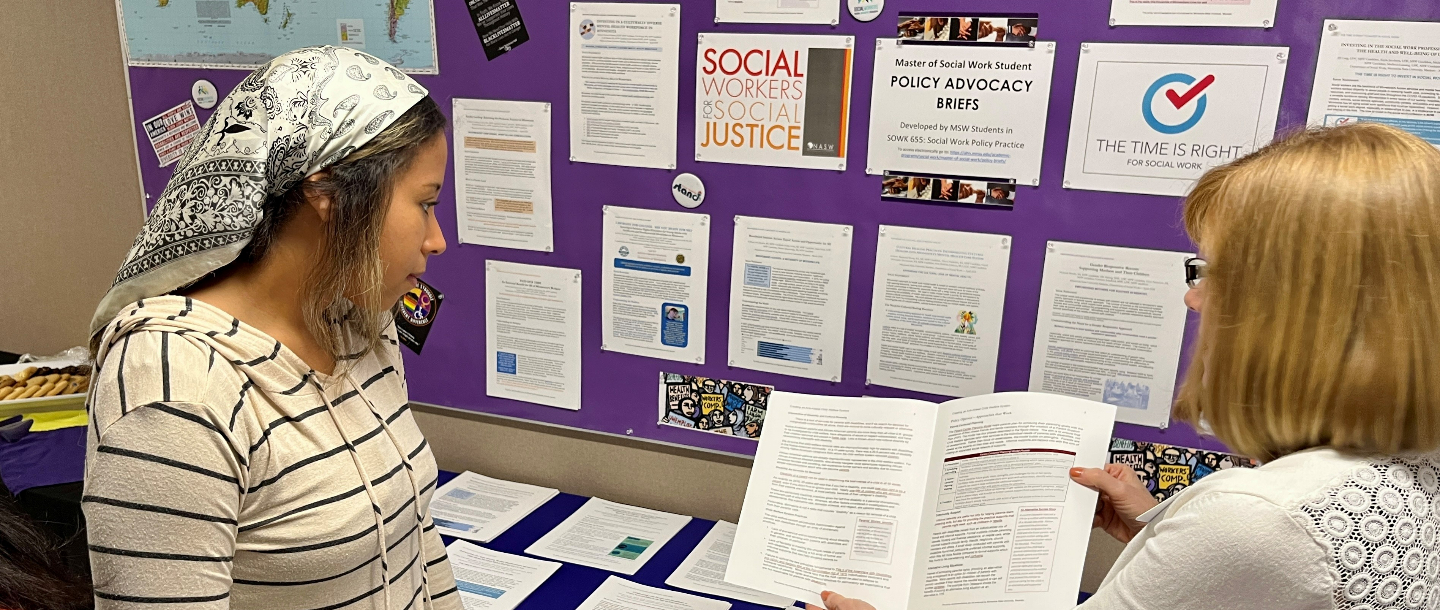 Student and faculty discussing and looking at a policy during an open house in the Social Work program