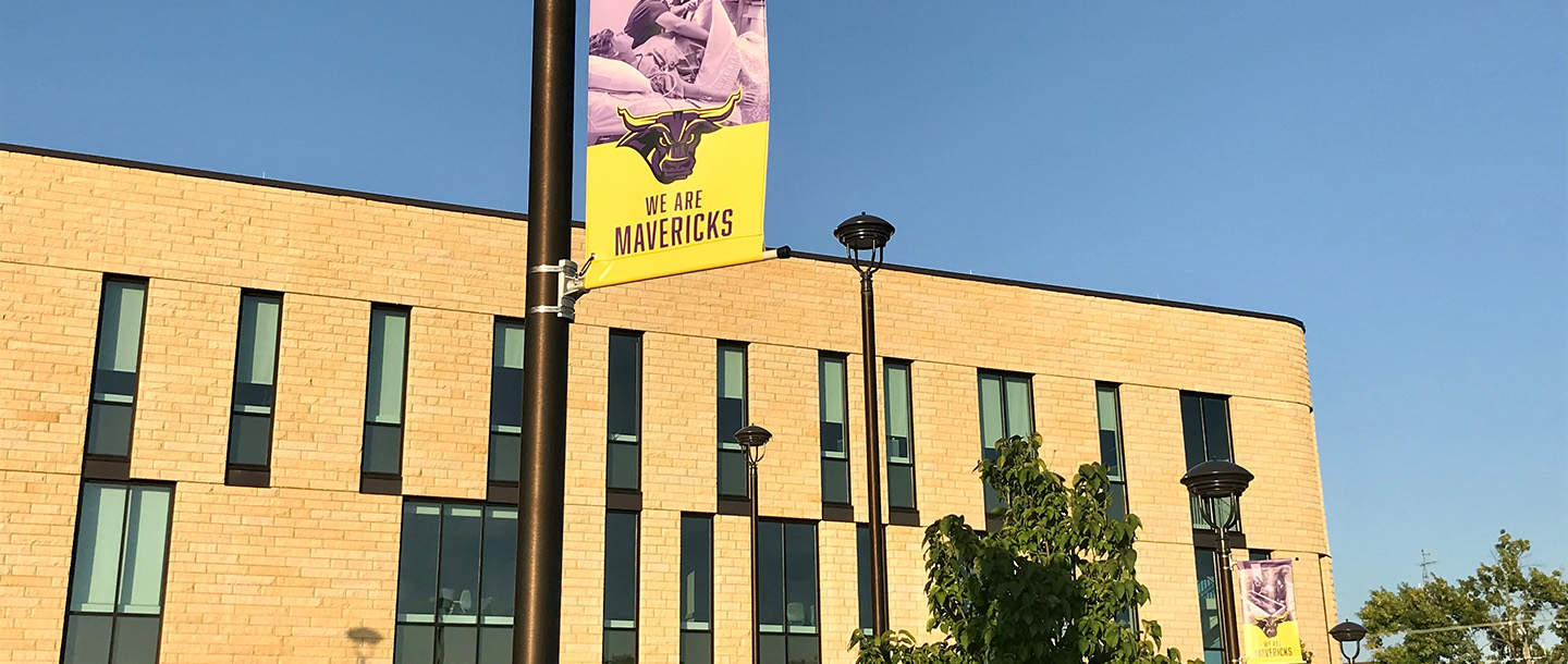 Flag on light pole that says We Are Mavericks outside of Clinical Sciences Building