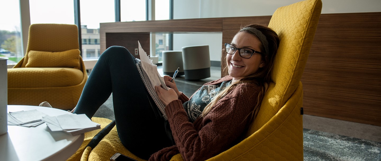 Student sitting in a chair with noteboook, studying and posing with a smile